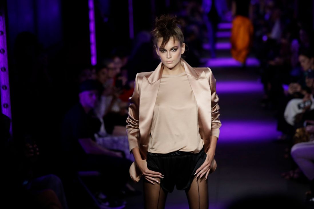 Kaia Gerber in a beige shirt and jacket and black shorts walks the catwalk for Tom Ford